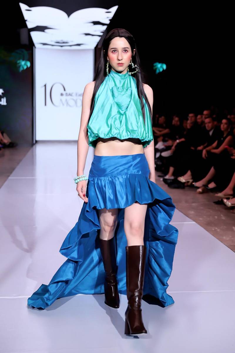 Este bello conjunto de dos piezas dramáticas: bubble top jade con cuello halter y corazón 3D central, evocando la exposición del corazón como ofrenda sagrada, combinado con falda asimétrica azul maya, corta al frente y larga con cola posterior, con vuelo fruncido que aporta movimiento y teatralidad.
