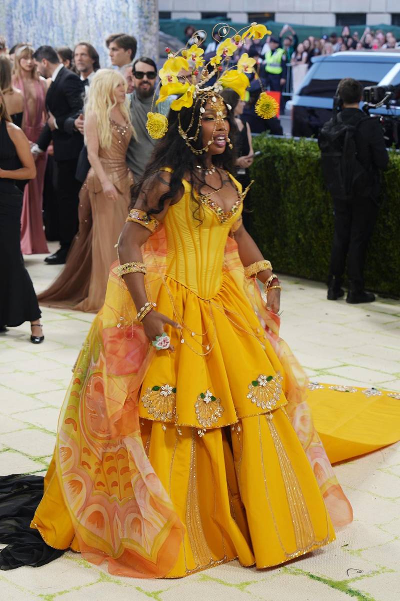 SZA llegó a la Met Gala 2026 como un rayo de sol convertido en fantasía. Su look, firmado por Bode, fue una de las interpretaciones más poéticas de la noche. El diseño partía de un corset estructurado y una falda arquitectónica en tonos amarillo dorado, construidos a partir de más de 100 yardas de textiles vintage, ensamblados como un collage cargado de historia y sostenibilidad.