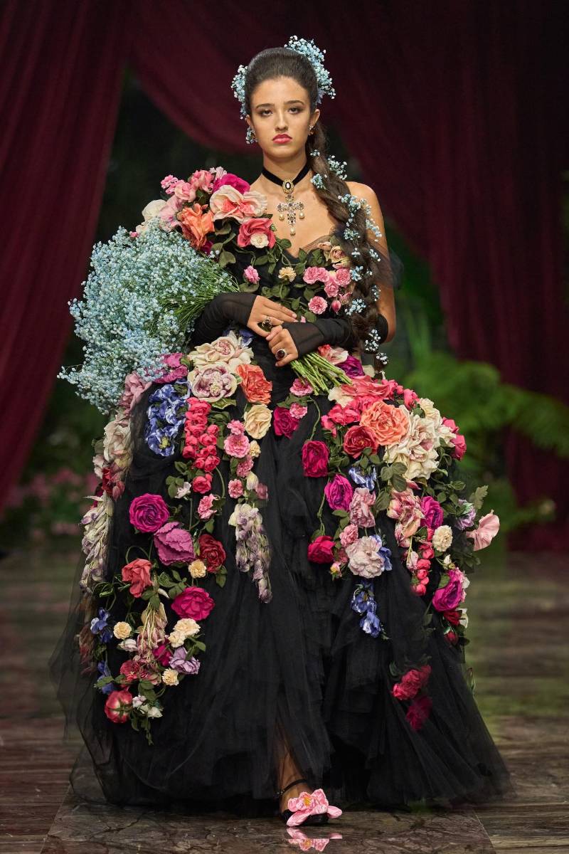 Léonie Cassel, la hija de Monica Bellucci y Vincent Cassel, dio inicio al desfile en un fascinante vestido de baile de tul decorado con una variedad de flores, llevando un ramo azul de velo de novia entre sus manos. Su madre estaba presente entre el público, sentada junto a Jennifer Lopez.