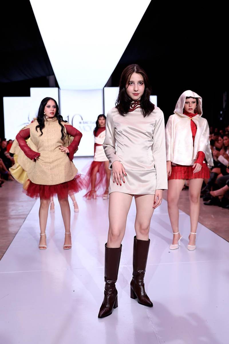 Y cerrando con broche de oro, la diseñadora Rosangel Donaire lució un vestido de satín gris claro con corte a la cadera, cuello alto y tiras de chiffon rojo que se anudan en la espalda. El diseño incluye un elegante cut-out posterior decorado con una cadena dorada