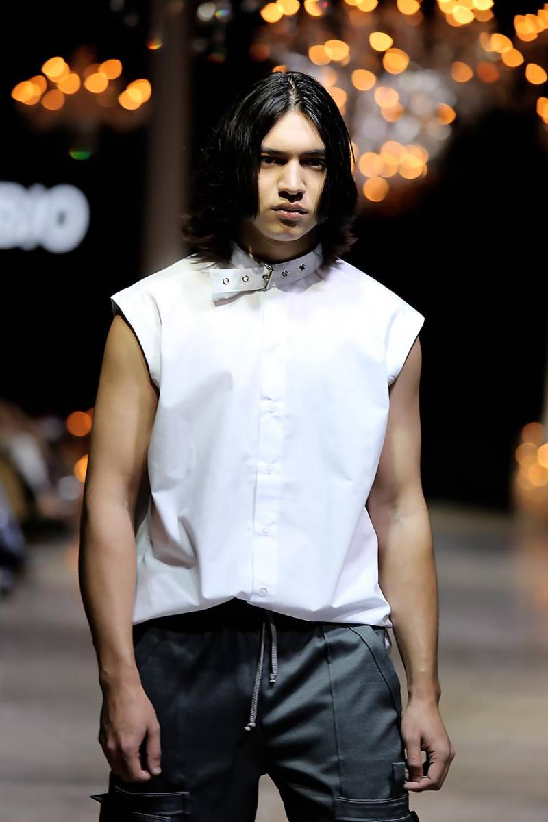 El blanco es el color predominante junto al gris que evoca el hormigón al descubierto. Camisa de botones con cuello de correa con hebilla metálica.