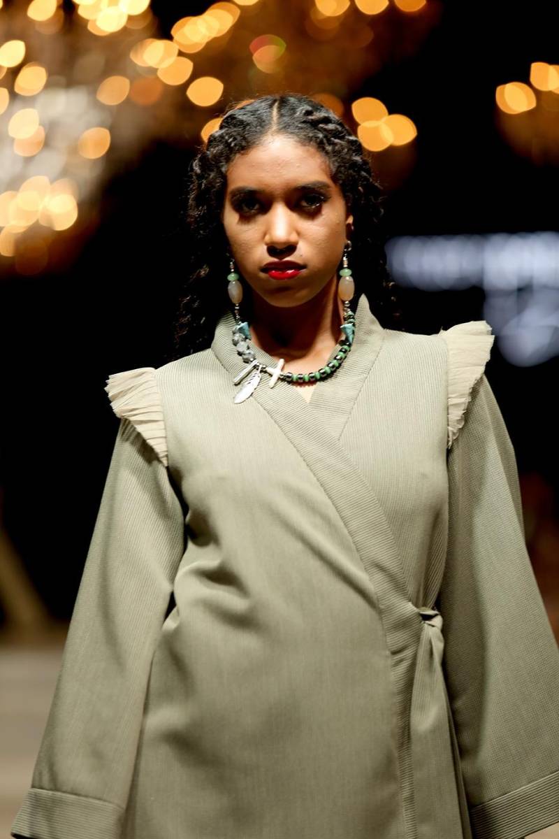 Vestido cruzado con ruffles en los hombros y collar de piedras con dijes colgantes y aretes a tono.