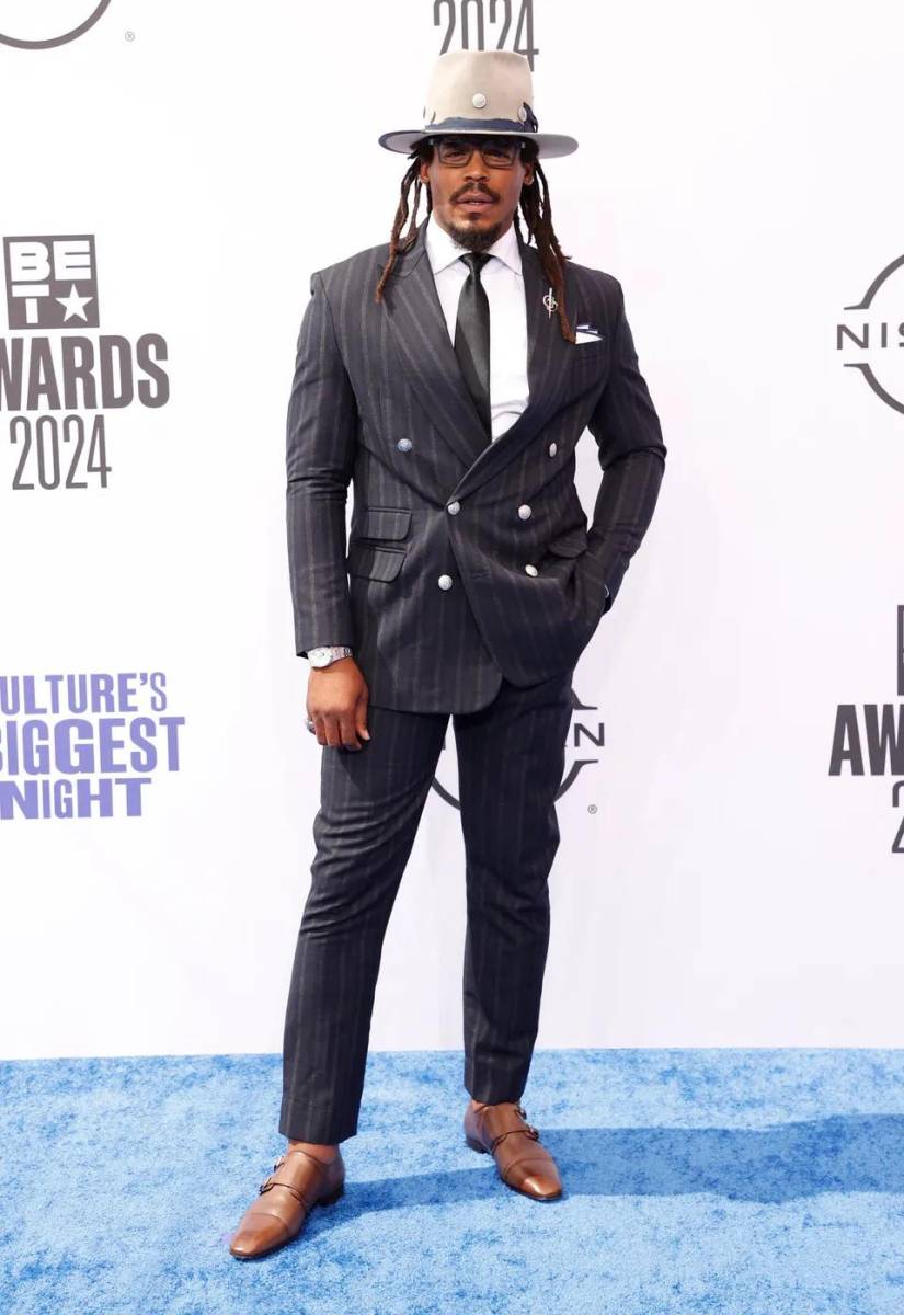 Cam Newton vistió un traje negro con líneas combinado con un sombreo café.