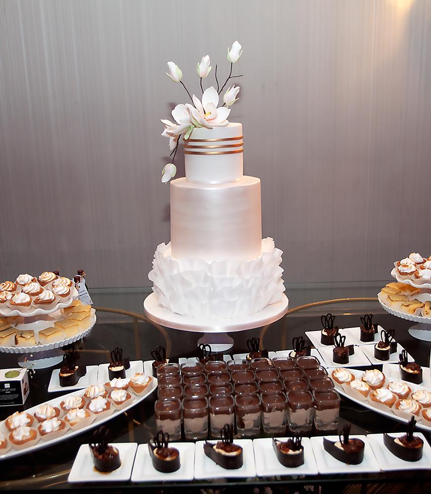 Pastel de boda de 3 niveles decorado con pétalos en la base y un ramo de flores y botones, elaborado por Signature Cakes.