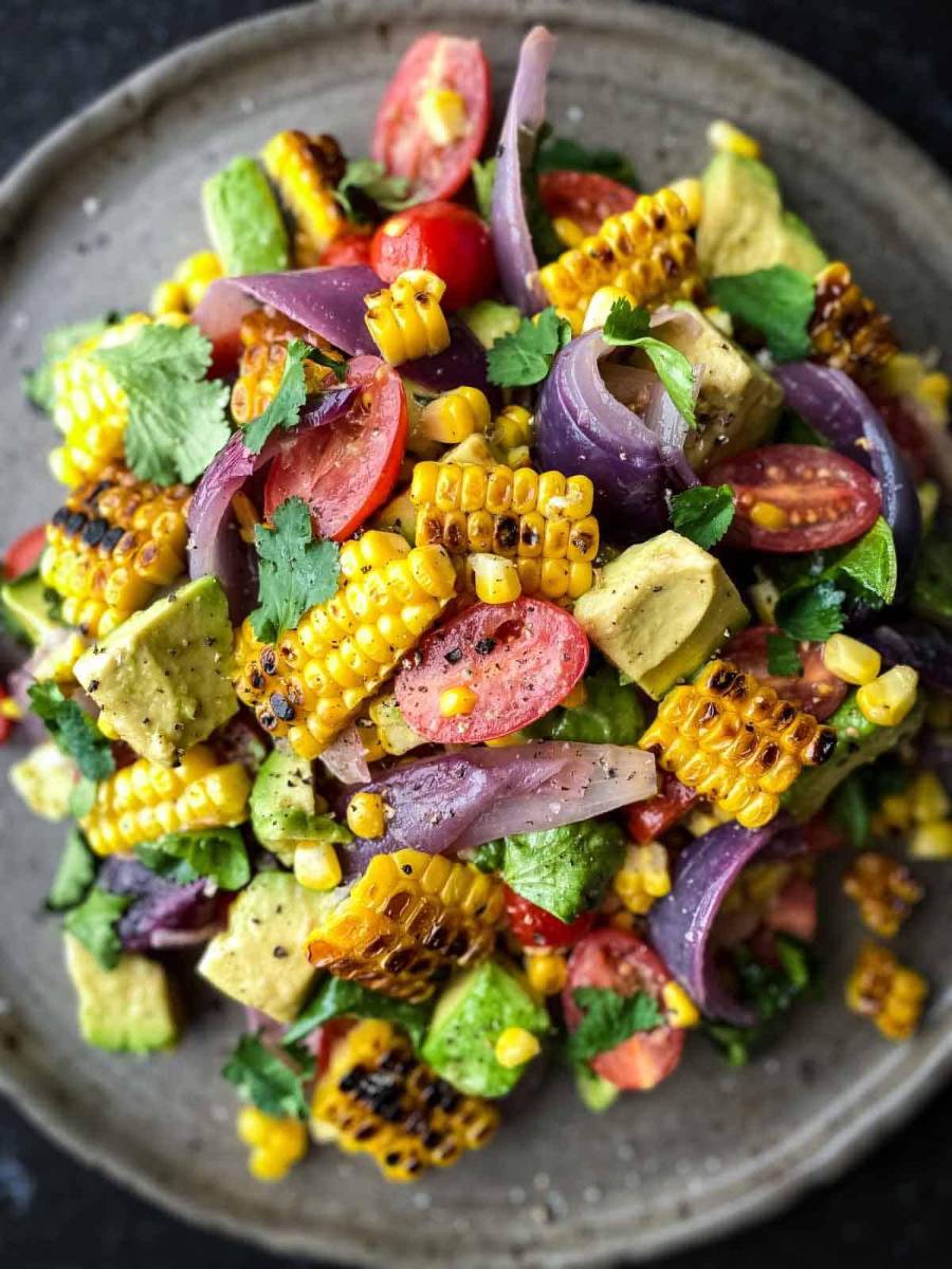 Ensalada de aguacate, maíz tostado y cebolla roja asada reúne todos los sabores frescos en un mismo plato. La combinación de maíz dulce y ahumado con aguacate, tomates cherry, cebolla roja asada y un aliño de limón y mostaza de Dijon la convierte en la guarnición perfecta para cualquier barbacoa o reunión de comida compartida.