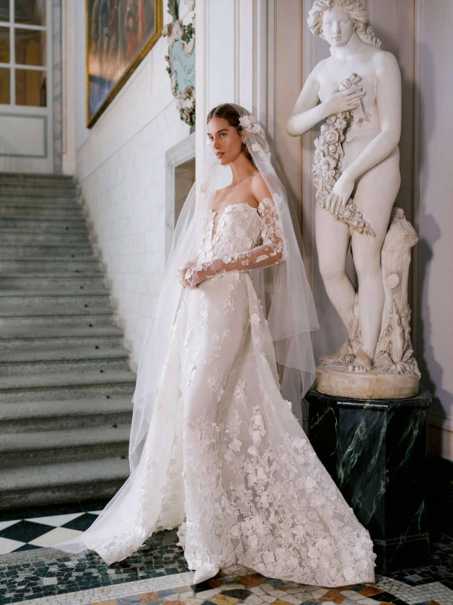 Vestido columna sin tirantes de encaje floral tridimensional con escote corazón profundo y cola de sobrefalda. Combinado con guantes largos de ópera de encaje floral a juego